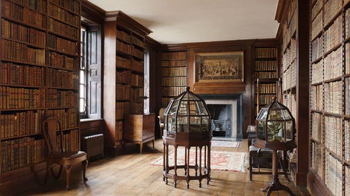 A view across the library at Dunham Massey, including shelves of historic books and a large wood carving on the wall.